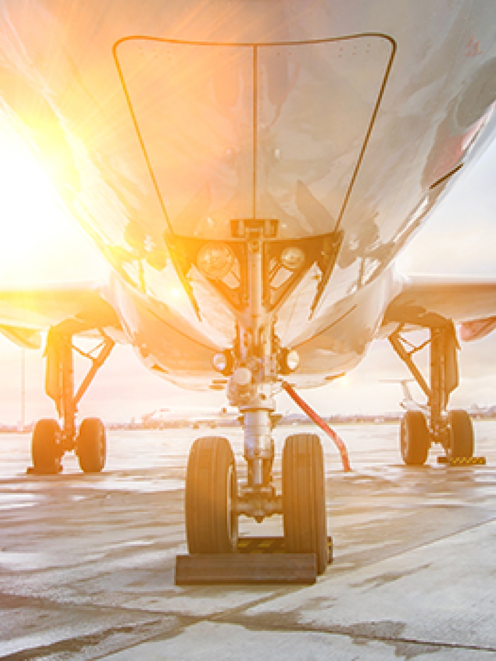 ue de face d’un avion sur une piste d’aéroport, montrant le train d’atterrissage, les deux moteurs et un soleil éclatant se reflétant sur le fuselage.