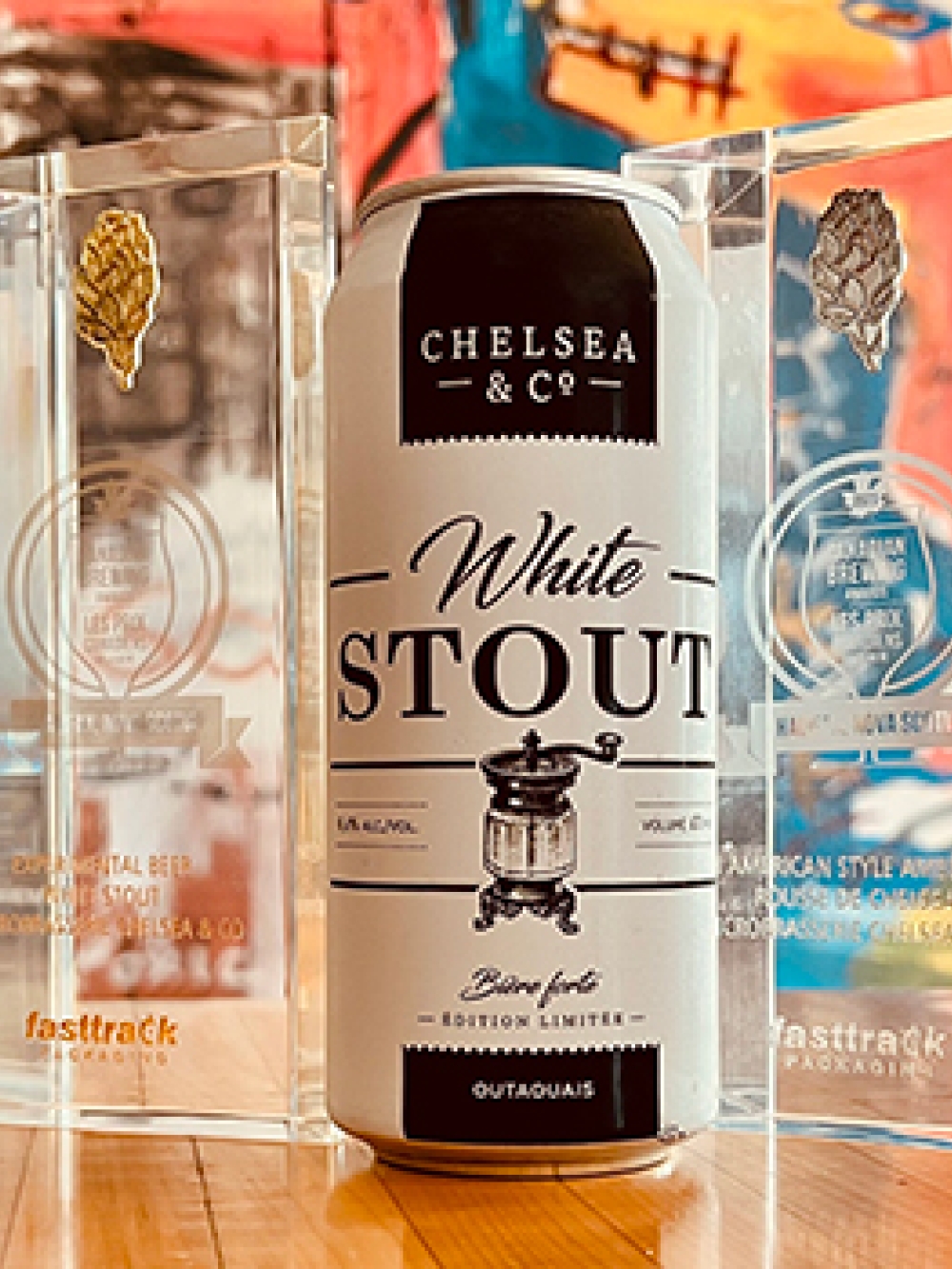 Canettes de bières de la Microbrasserie Chelsea & Co. exposées sur une table, entourées de trophées transparents mettant en valeur les prix remportés.