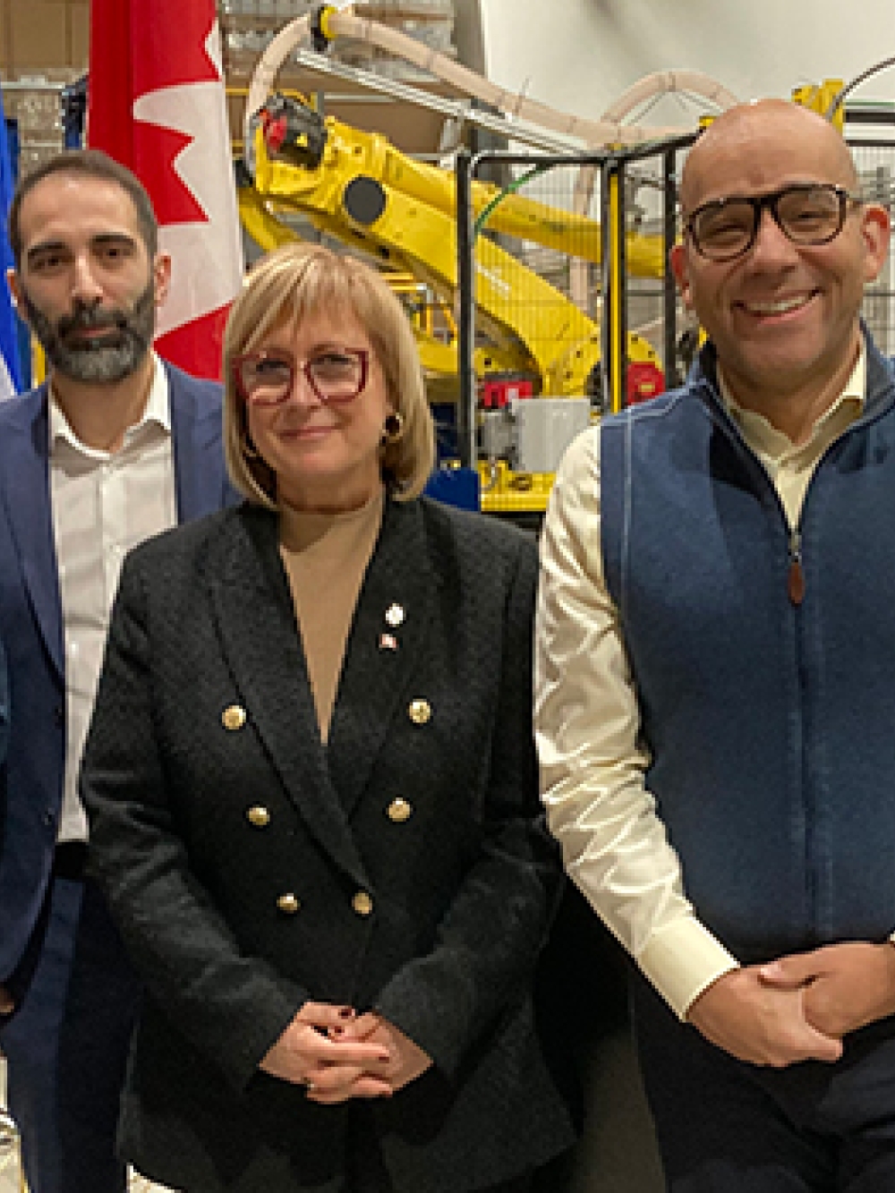 Groupe de cinq personnes posant à l’intérieur d’une usine devant des bannières et des drapeaux, avec de l’équipement industriel en arrière-plan.