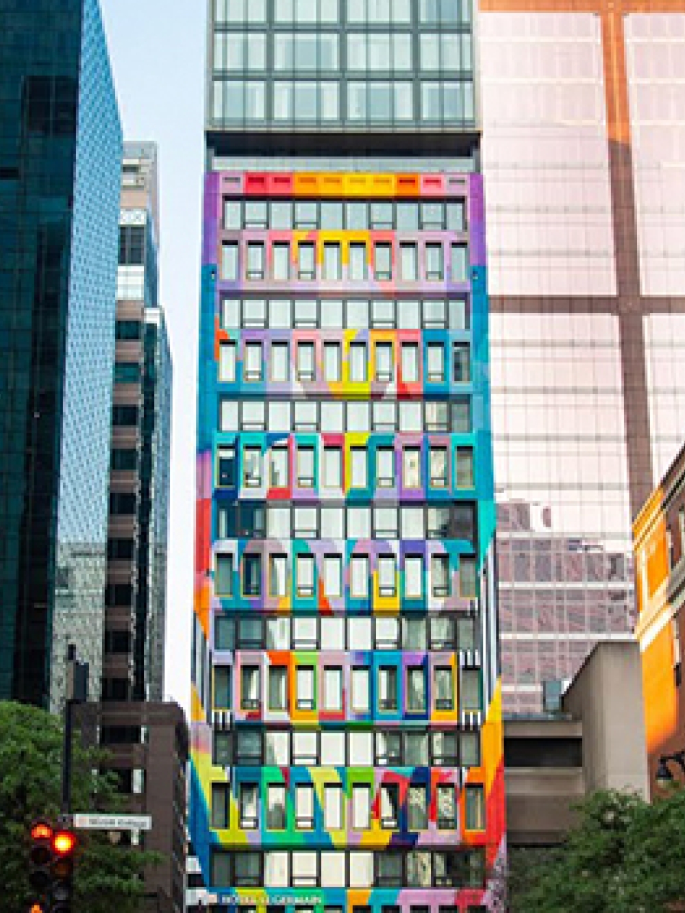 Façade d’un immeuble étroit aux fenêtres colorées au centre-ville, entouré de gratte‑ciel aux tons gris et vitrés.