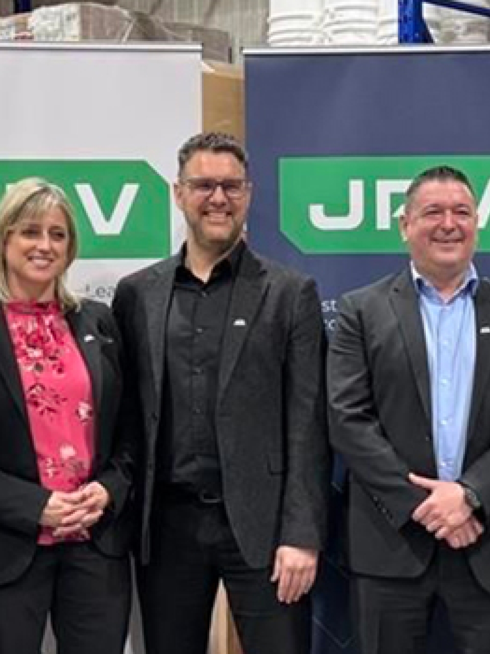 Groupe de cinq personnes en tenue professionnelle posant devant deux bannières JRV dans un environnement d’entrepôt.