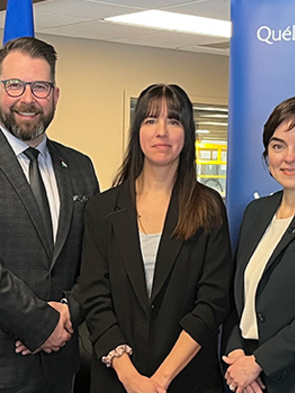 Groupe de cinq personnes posant à l’intérieur devant des fenêtres exposées et une bannière du gouvernement du Québec.