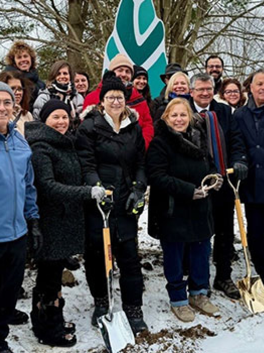 Grand groupe de personnes rassemblées à l’extérieur en hiver, tenant des pelles dorées pour une cérémonie de première pelletée de terre, devant un drapeau associé à la Fondation Gisèle-Faubert.