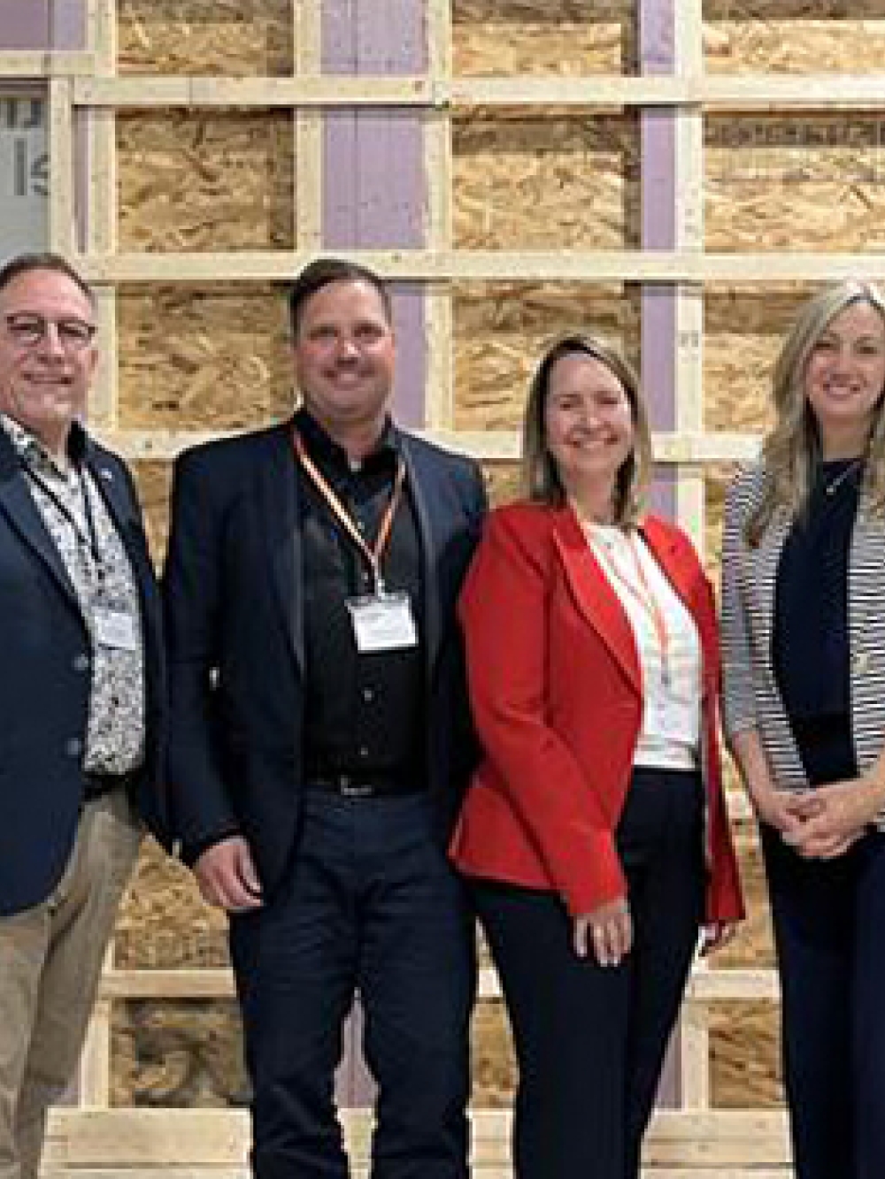 Groupe de personnes posant devant une structure murale en construction, accompagnées des drapeaux du Québec et du Canada, lors d’un événement officiel à l’usine Prestige Panel.
