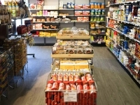 Rayon d’épicerie avec des étagères remplies de produits alimentaires et ménagers, incluant des conserves, des bouteilles, des boîtes et des paniers de produits au centre de l’allée.