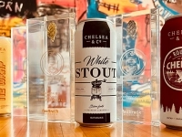 Canettes de bières de la Microbrasserie Chelsea & Co. exposées sur une table, entourées de trophées transparents mettant en valeur les prix remportés.