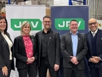 Groupe de cinq personnes en tenue professionnelle posant devant deux bannières JRV dans un environnement d’entrepôt.