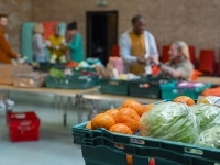  Bacs remplis de fruits et légumes frais dans une salle où des personnes préparent et distribuent des denrées alimentaires.