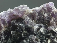 Grosse roche brute composée de cristaux aux teintes violettes, noires et blanches, montrant une texture minérale détaillée.