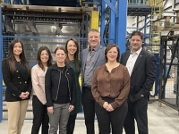 Groupe de personnes debout dans une usine devant de grands équipements industriels bleus et jaunes, posant pour une photo officielle.