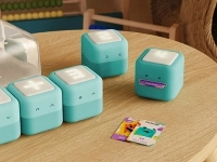 Petits cubes de jeu PLAYCubes disposés sur une table, accompagnés de cartes colorées et d’un étui de rangement à l’arrière.