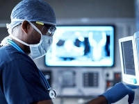 Un professionnel de la santé en salle d’opération utilise des appareils médicaux, avec un écran affichant des images radiologiques. 