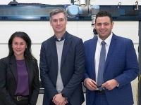 Trois personnes debout dans un environnement industriel, devant un équipement automatisé composé d’une structure métallique, de capteurs et d’un bras robotisé. 